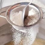 sifting flour into creamed butter, sugar, eggs, and vanilla in a stand mixer bowl.
