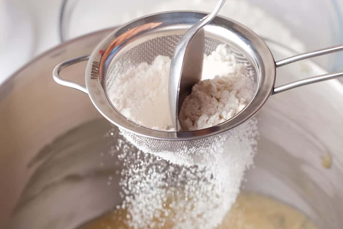 sifting flour into creamed butter, sugar, eggs, and vanilla in a stand mixer bowl.