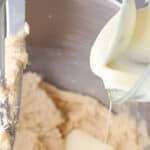 pouring melted white chocolate into blondie batter in a stand mixer with the paddle attachment.