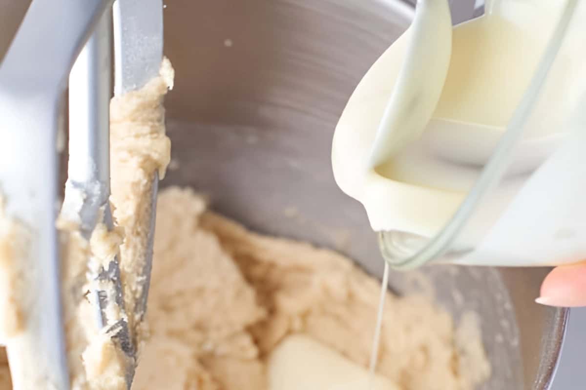 pouring melted white chocolate into blondie batter in a stand mixer with the paddle attachment.