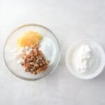 crushed pineapple, pudding mix, chopped nuts, and mini marshmallows in a bowl next to a bowl of whipped topping.