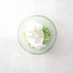 adding whipped topping to pistachio fruit and nut salad in a glass bowl.
