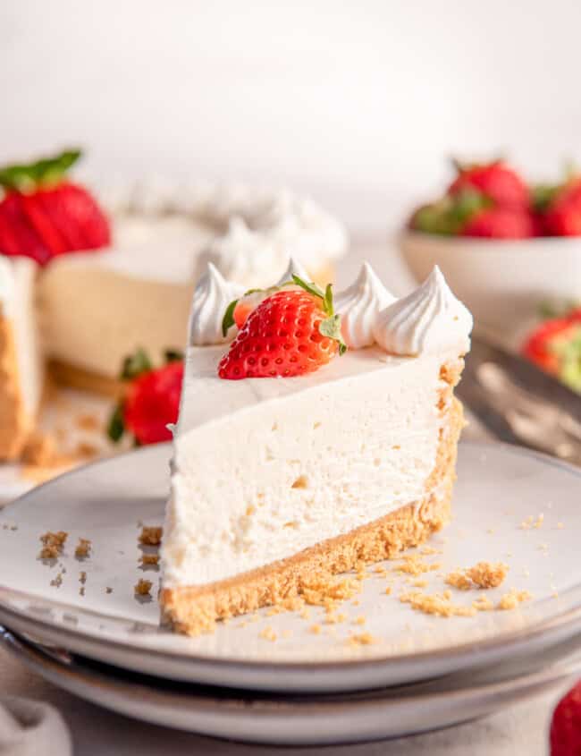 a slice of no bake cheesecake on a white plate topped with whipped cream and a strawberry.