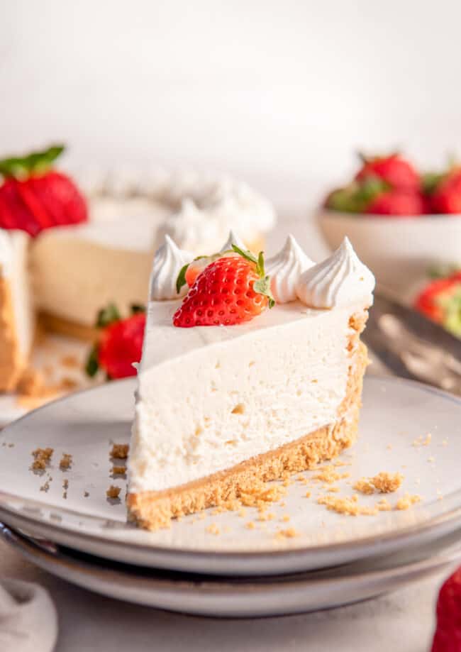 a slice of no bake cheesecake on a white plate topped with whipped cream and a strawberry.