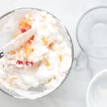 ambrosia salad being gently mixed with a rubber spatula in a glass bowl.