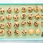 27 coconut chocolate chip cookie dough balls on a blue baking sheet with chocolate chips pressed into them.