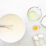 a bowl of flour and eggs with a whisk.