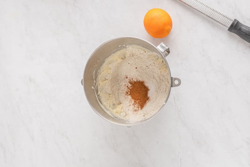 dry ingredients in a mixing bowl, next to an orange and zester tool