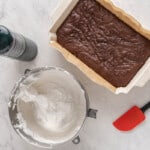 a brownie in a pan with a white substance in it next to a container with a red spatula.