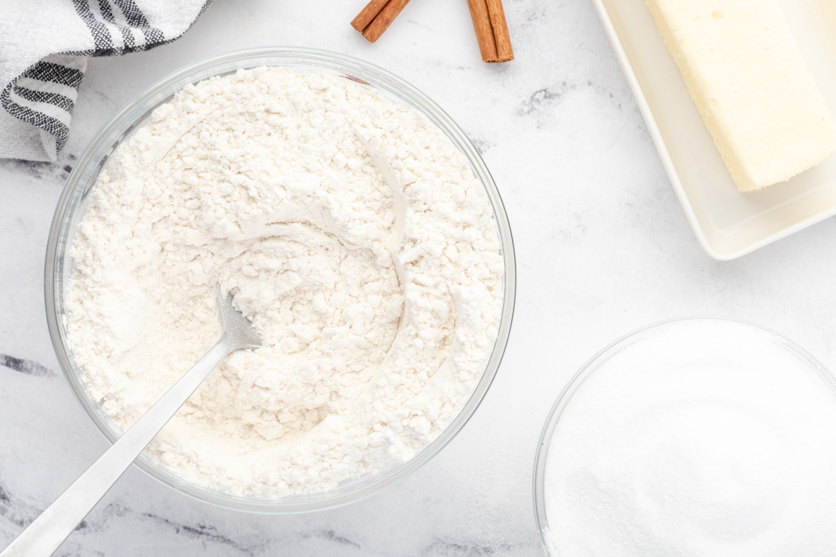 a bowl of flour, sugar and cinnamon next to a spoon.