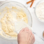 pouring buttermilk into cupcake batter in a glass bowl.