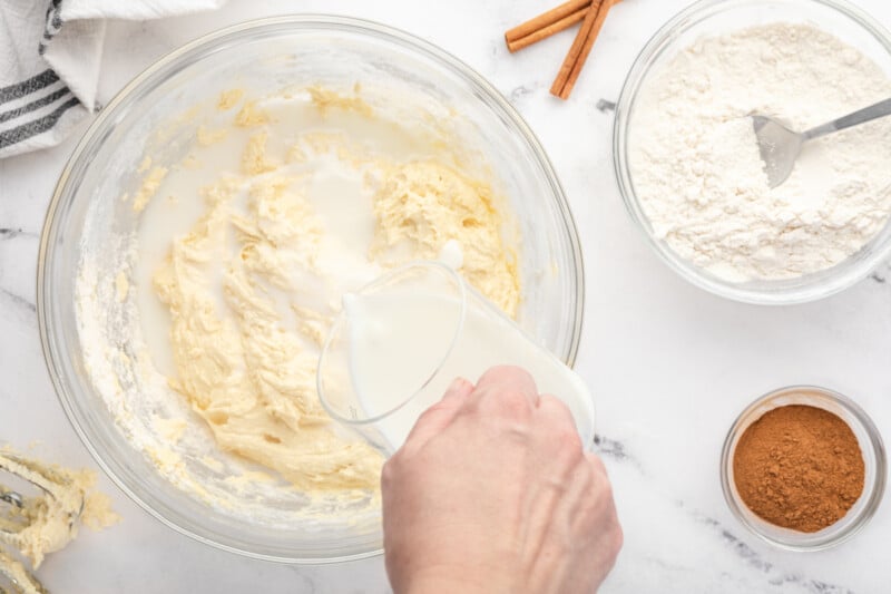 pouring buttermilk into cupcake batter in a glass bowl.