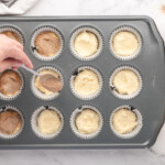 spooning cinnamon sugar over half-filled cupcakes in a lined cupcake tin.