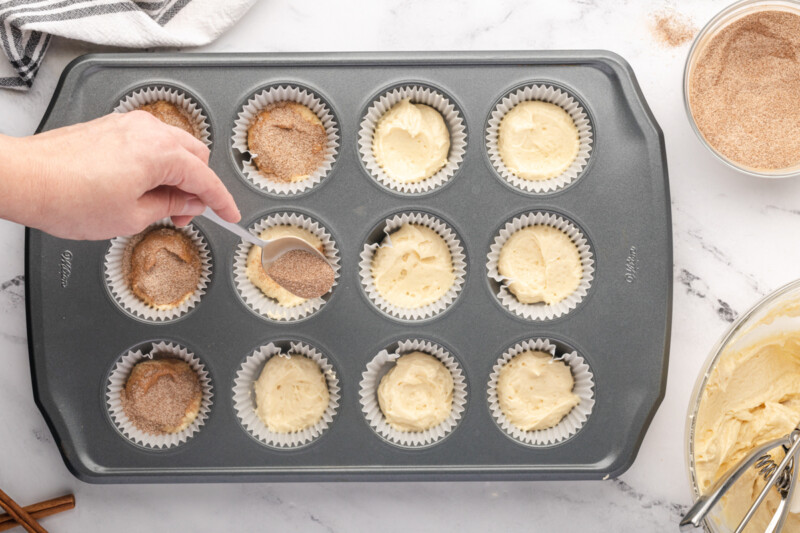 spooning cinnamon sugar over half-filled cupcakes in a lined cupcake tin.