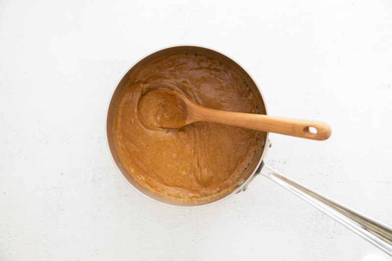 a brown sauce in a pan with a wooden spoon.