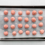 24 strawberry cake truffle balls on a baking sheet.