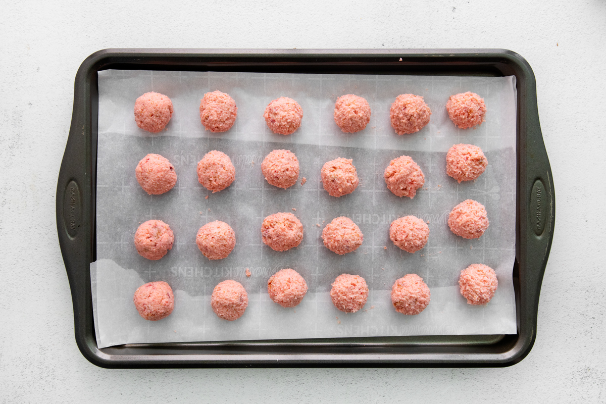 24 strawberry cake truffle balls on a baking sheet.
