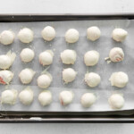 24 chocolate dipped strawberry cake truffles on a baking sheet.