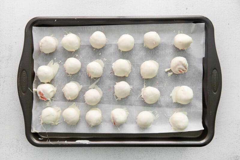 24 chocolate dipped strawberry cake truffles on a baking sheet.