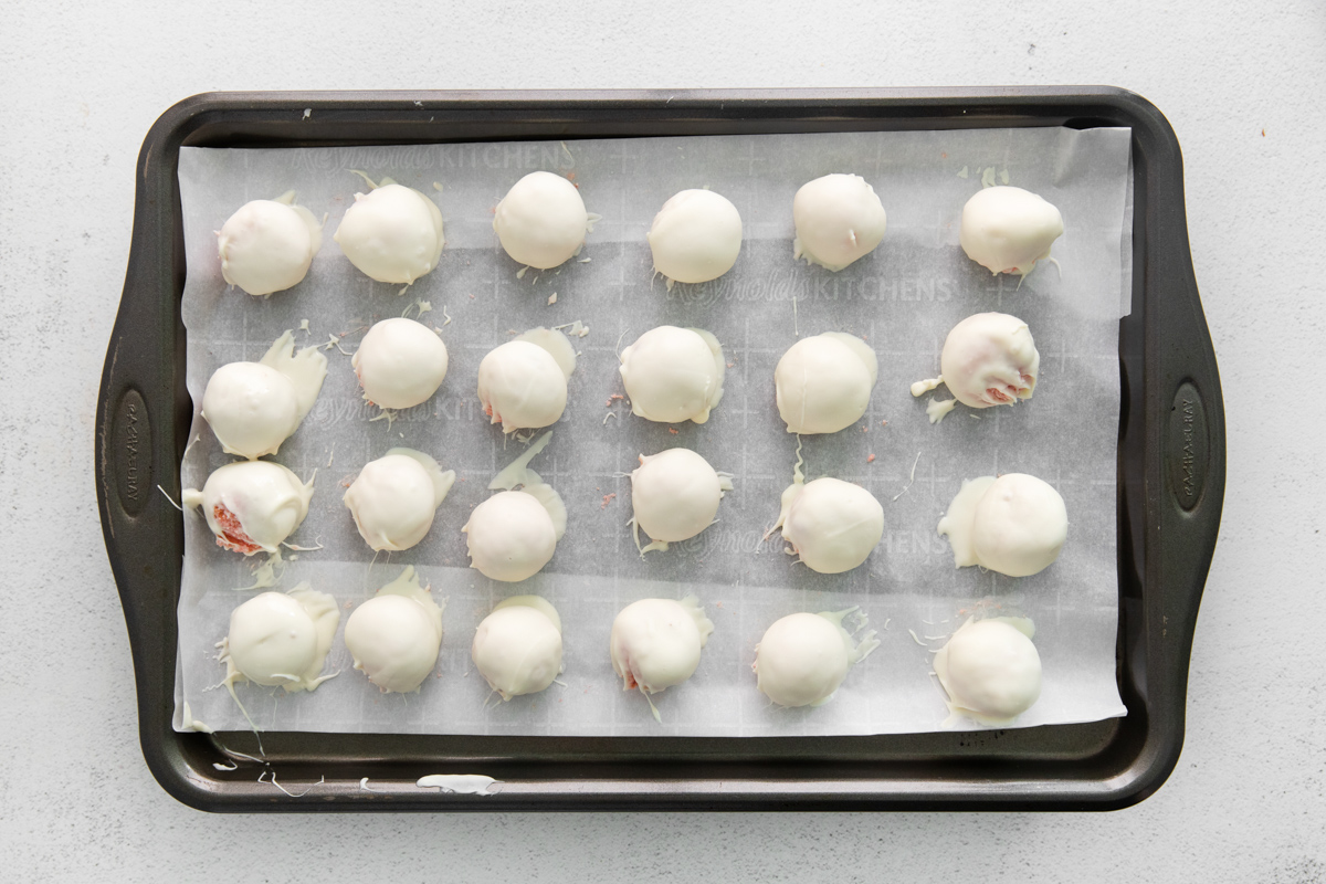 24 white chocolate dipped strawberry cake truffles on a baking sheet.