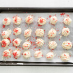 24 freeze-dried strawberry coated strawberry cake truffles on a baking sheet.