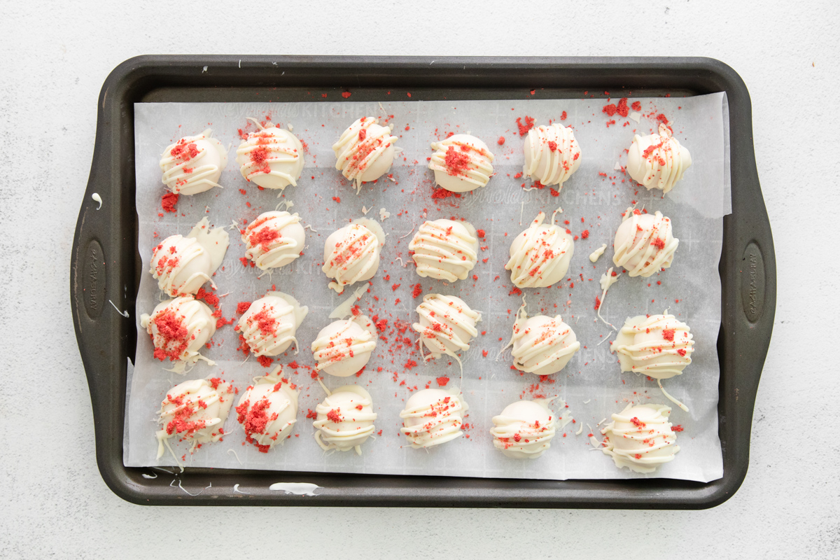 24 freeze-dried strawberry coated strawberry cake truffles on a baking sheet.