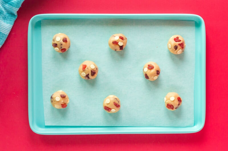 8 strawberry cheesecake cookie dough balls on a blue baking sheet.