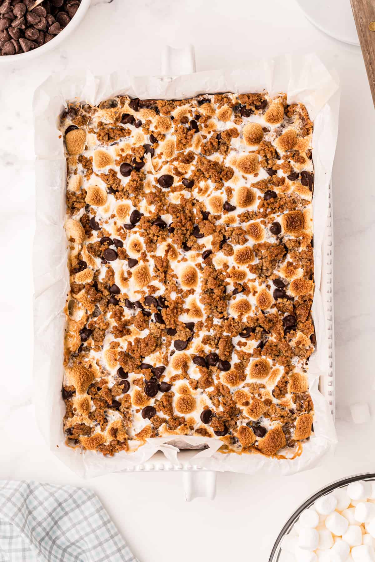 a baking dish full of s'mores bars, topped with marshmallow, chocolate chips, and graham cracker crumbles 