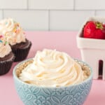 a bowl of cupcakes with whipped cream and strawberries.