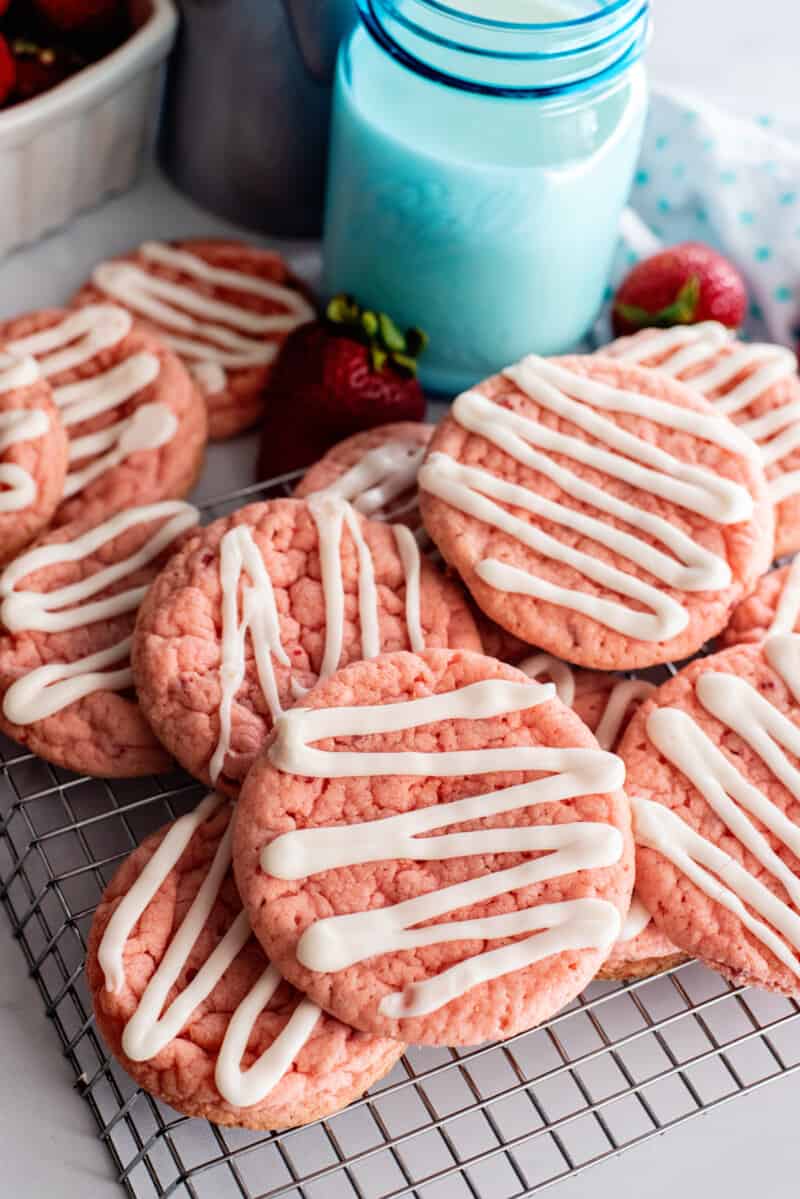 stacked strawberry cookies on a wire rack with a glass of milk.