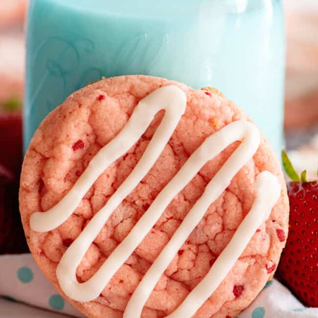 close up of a strawberry cookie leaned up against a glass of milk.