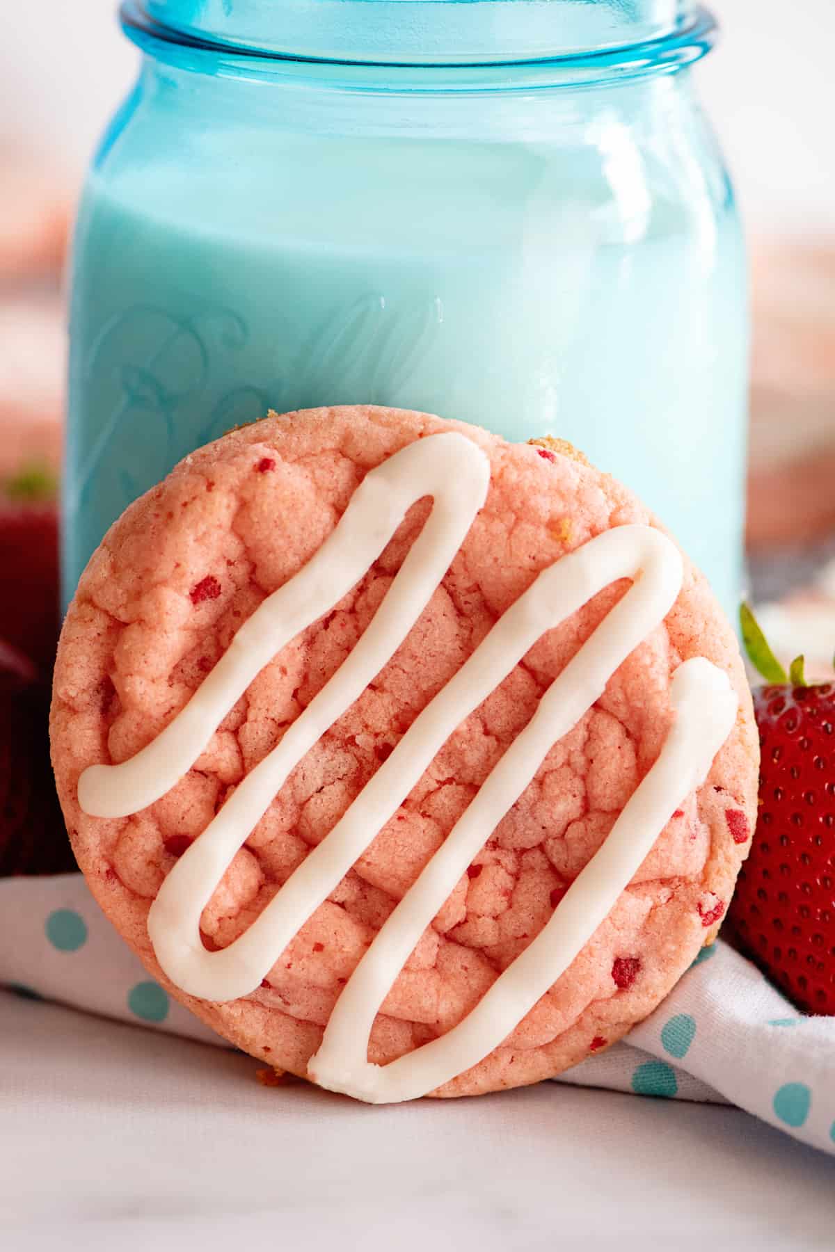 close up of a strawberry cookie leaned up against a glass of milk.