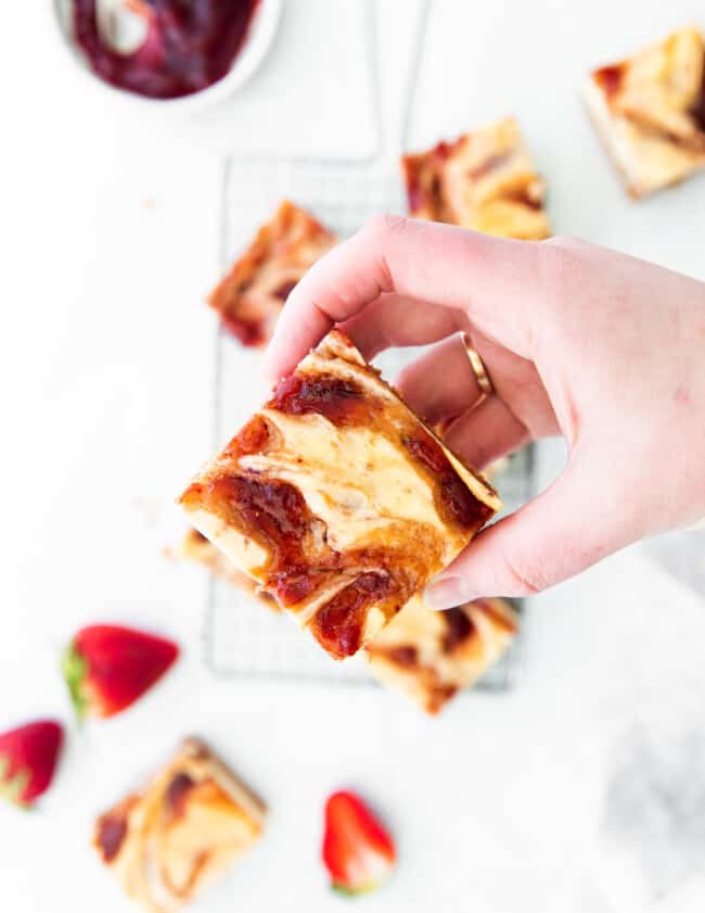 overhead view of a hand holding a strawberry cheesecake bar.