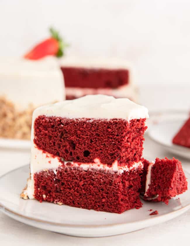 side view of a partially eaten slice of red velvet cake on a white plate.