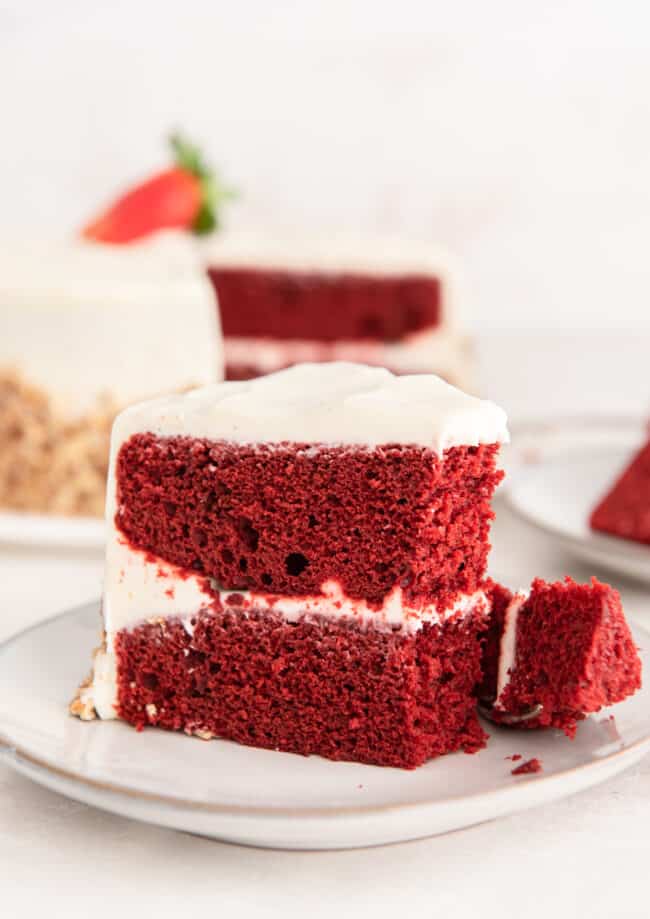 side view of a partially eaten slice of red velvet cake on a white plate.