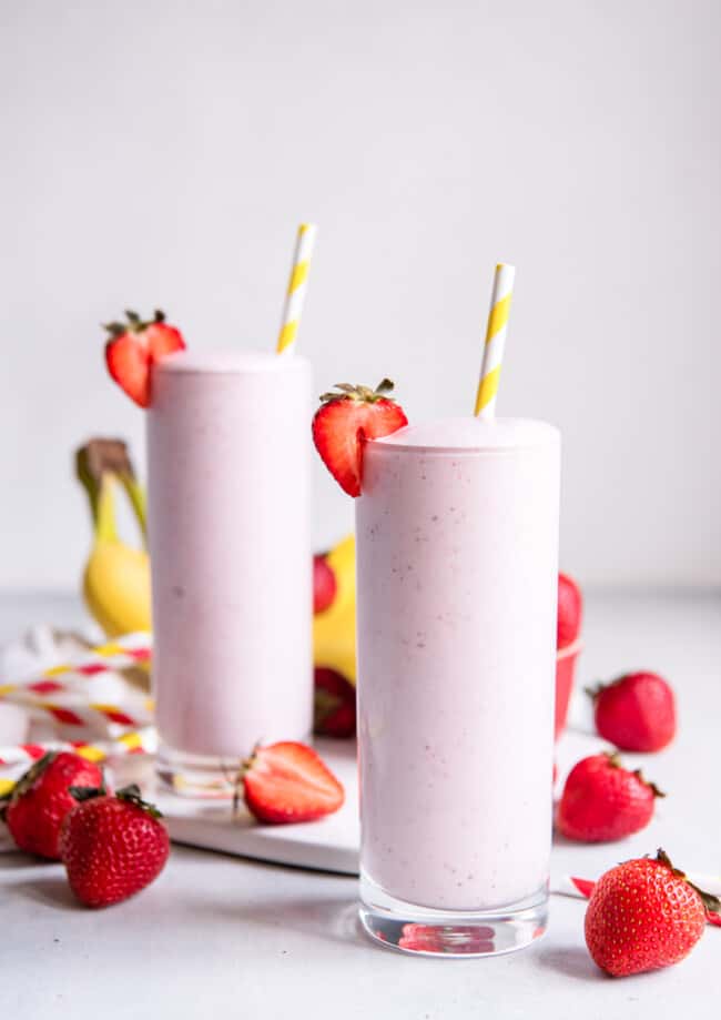 two glasses of milkshakes with straws and strawberries.