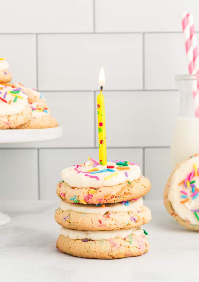 side view of a 3 stack of birthday cookies topped with a multicolor lit candle.