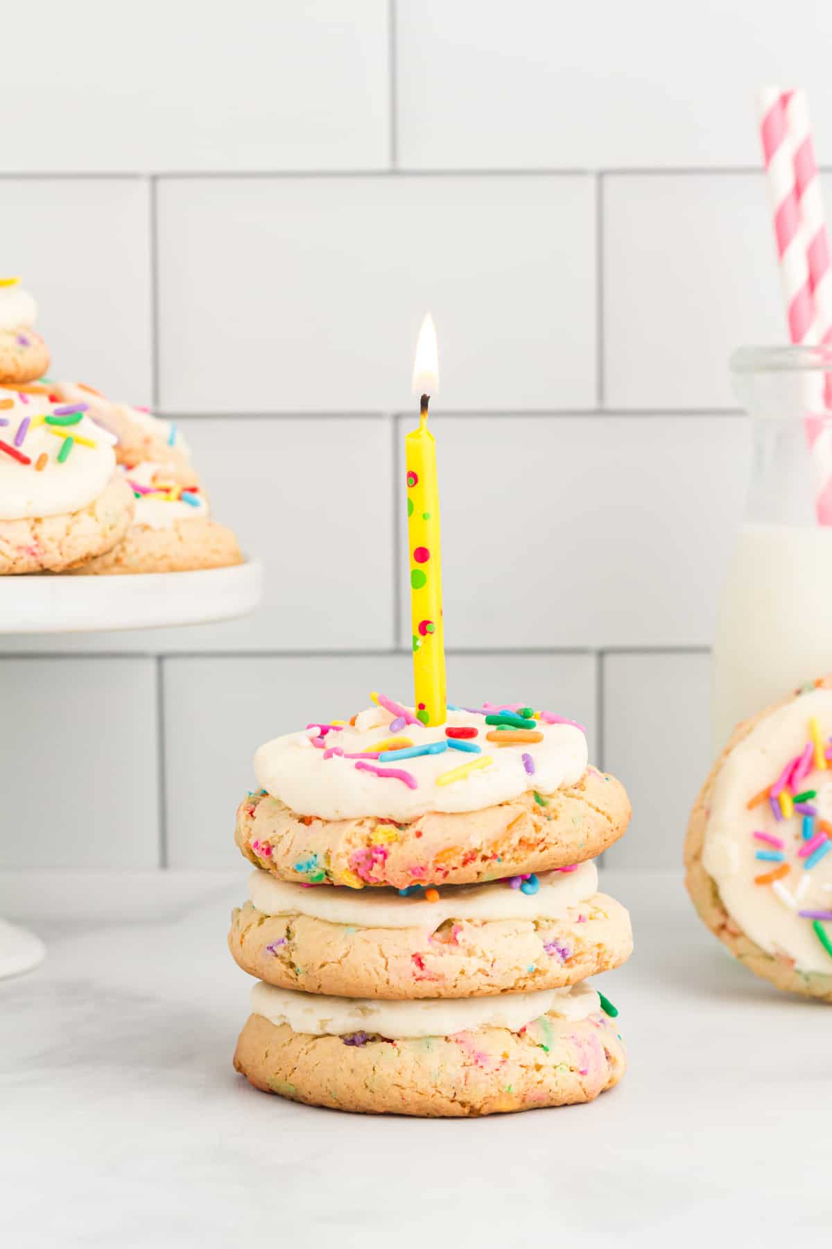 side view of a 3 stack of birthday cake cookies topped with a multicolor lit candle.