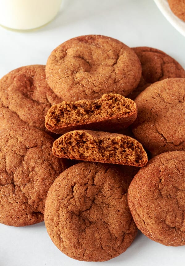 three-quarters view of gingersnap cookies in a pile on a white counter, one is halved and stacked on itself to show the interior texture.