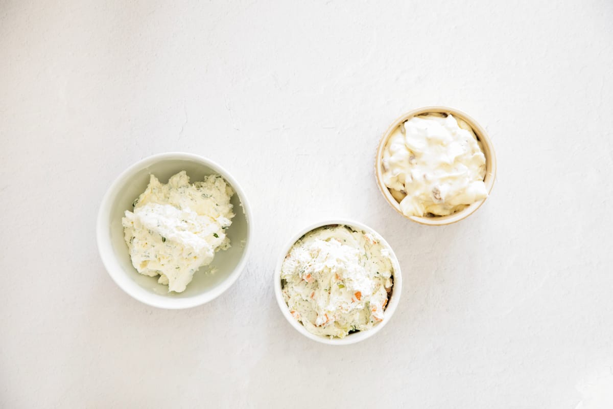 Homemade flavored cream cheese spreads in small dishes.