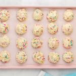 20 birthday cookie dough balls on a pink baking sheet.