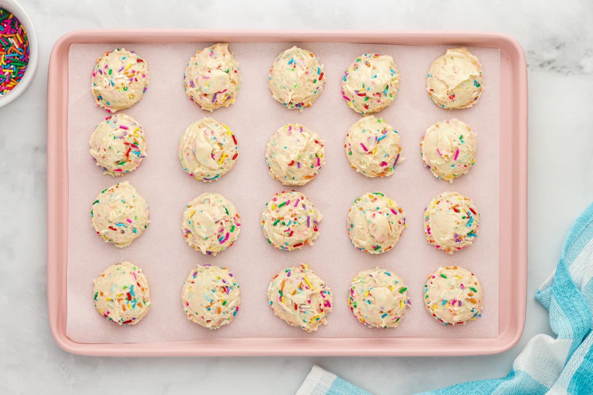 20 birthday cookie dough balls on a pink baking sheet.