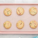 6 baked birthday cookies on a pink baking sheet.