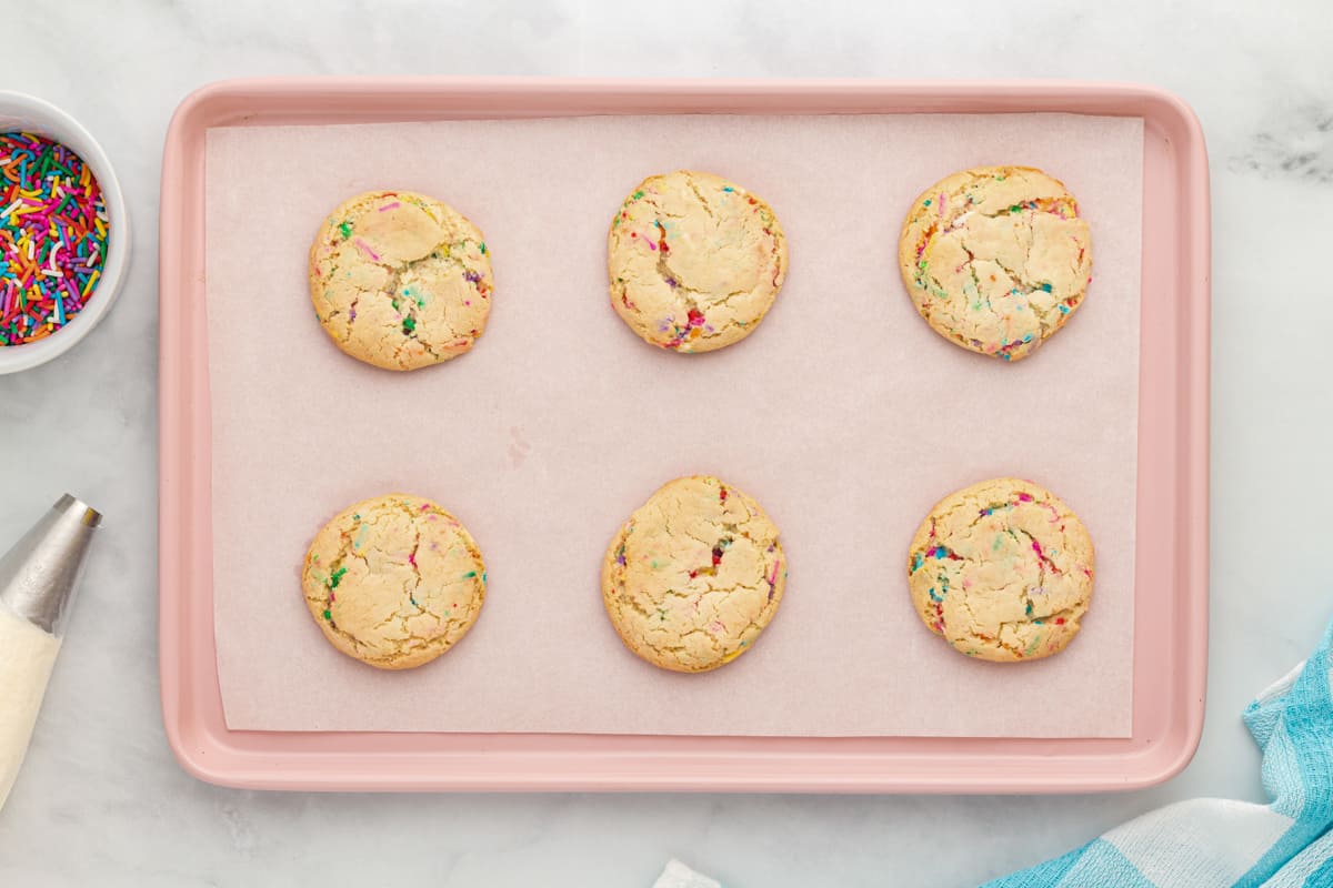 6 baked birthday cookies on a pink baking sheet.