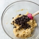 chocolate chips folded into gluten free chocolate chip cookie dough in a glass bowl with a rubber spatula.