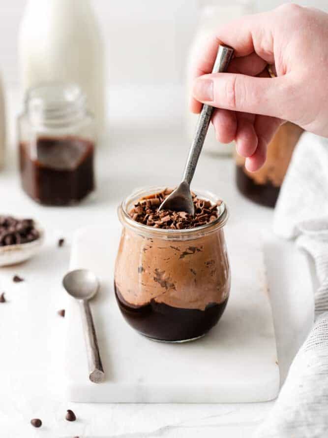 three-quarters view of a hand dipping a spoon into a no bake chocolate cheesecake cup.