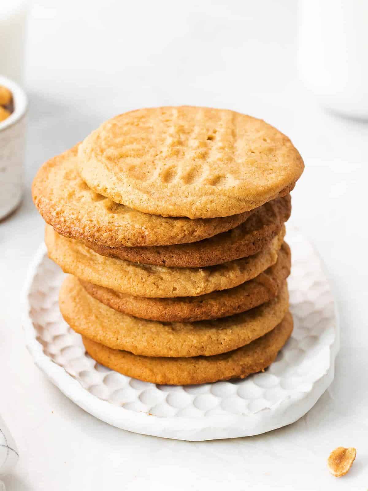 side view of 7 brown butter peanut butter cookies stacked on a white plate.