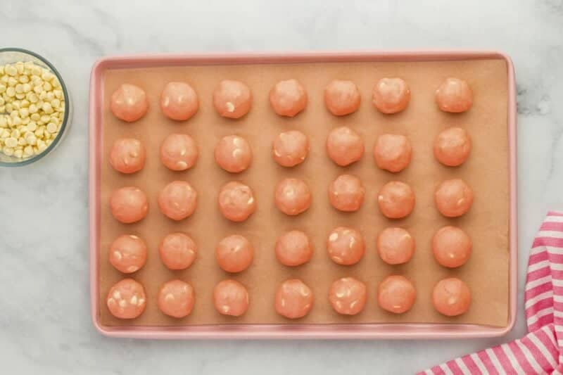 strawberry white chocolate chip cookie dough balls on a lined baking sheet.