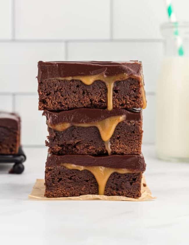 side view of 3 stacked caramel brownies on a square of parchment paper.