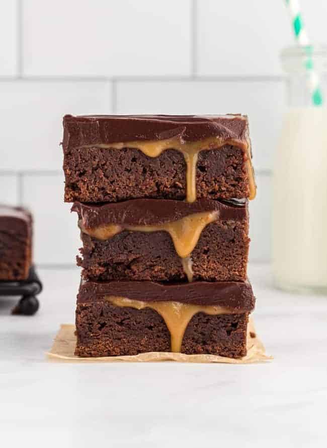 side view of 3 stacked caramel brownies on a square of parchment paper.